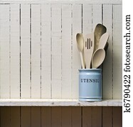 Kitchen cooking utensils; wooden spatulas etc in china storage pot; on wooden shelf against rustic kitchen wall; excellent copy space over wall area Kitchen cooking utensils; wooden spatulas etc in china storage pot; on wooden shelf against rustic kitchen wall; excellent copy space over wall area