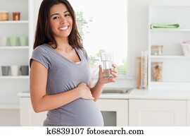 Attractive pregnant woman holding a glass of water while standind