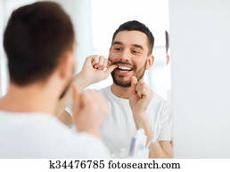man with dental floss cleaning teeth at bathroom man with dental floss cleaning teeth at bathroom