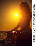 woman meditating in lotus pose on the beach at sunset