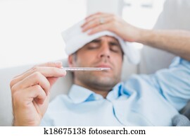 Sick man lying on sofa checking his temperature Sick man lying on sofa checking his temperature