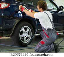 Serviceman polishing car body with machine in a workshop Serviceman polishing car body with machine in a workshop