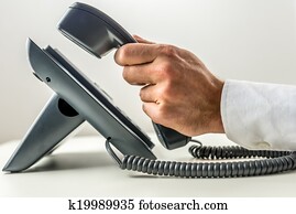 Male hand picking up the receiver of a telephone