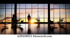 Business man standing in the office looking out of the window at sunset sky.