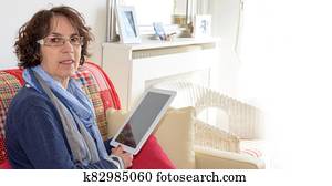 mature smiling woman with a digital tablet on a sofa mature smiling woman with a digital tablet on a sofa