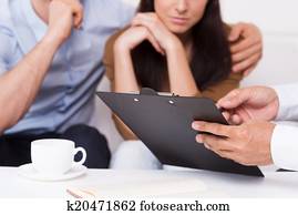 señal, here., primer plano, de, pensativo, pareja joven, sentar sofá, mientras, hombre, en, formalwear, señalar, portapapeles, con, documento