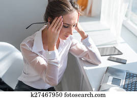 Portrait of tired young business woman suffering from headache in front laptop at office desk