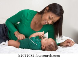ethnic mother playing with her baby boy son on bed