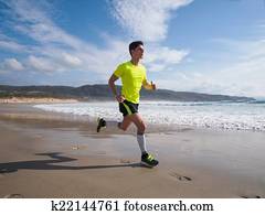 Young Man In Fitness Clothing Running Along Beach