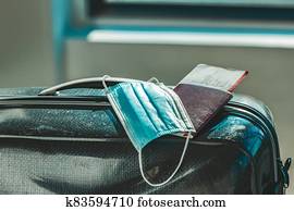 COVID-19 travel mask with luggage. Coronavirus airport restriction. A medical face mask with passport, plane ticket, suitcase and luggages COVID-19 travel mask with luggage. Coronavirus airport restriction. A medical face mask with passport, plane ticket, suitcase and luggages