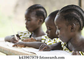 Two beautiful African girls and one African boy reading and writing at school as an educational symbol outside their school in Bamako, Mali. Beautiful education symbol background.