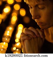 Prayer praying in Catholic church near candles. Religion concept.