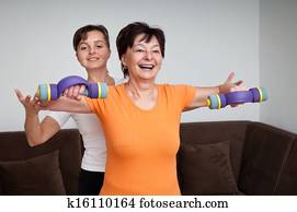 Coach assisting senior woman exercising with barbells