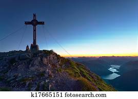 summit cross on mountain with lake in valley at sunrise 