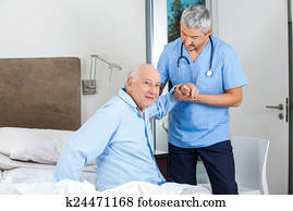Senior Man Being Assisted By Male Caretaker In Bedroom