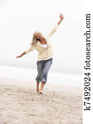 Senior Woman On Holiday Running Along Winter Beach
