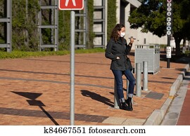 Caucasian woman wearing a protective mask out in the streets, using her phone Caucasian woman wearing a protective mask out in the streets, using her phone