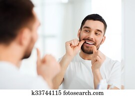 man with dental floss cleaning teeth at bathroom man with dental floss cleaning teeth at bathroom