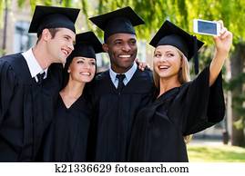Capturing a happy moment. Four college graduates in graduation gowns standing close to each other and making selfie Capturing a happy moment. Four college graduates in graduation gowns standing close to each other and making selfie