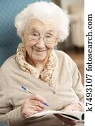 Senior Woman Relaxing In Chair At Home Completing Crossword
