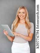 essai, elle, nouveau, gadget., sourire, jeune femme, travailler, tablette numérique, et, regarder appareil-photo, quoique, debout, contre, gris, fond