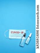 Disposable blue medical face mask with COVID-19 sign and alcohol hand sanitizer antiseptic on blue background Disposable blue medical face mask with COVID-19 sign and alcohol hand sanitizer antiseptic on blue background