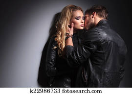 In love fashion couple kiss against a grey wall. In love fashion couple kiss against a grey wall.