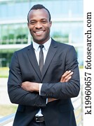 Confident and successful businessman. Handsome young African man in full suit keeping arms crossed and looking at camera while standing outdoors