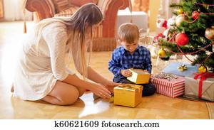  young woman giving Christmas gifts to her little boy on Christmas morning
