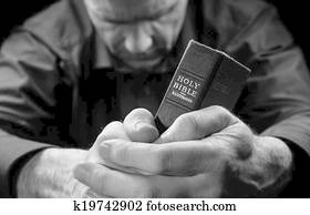 A Man praying holding a Holy Bible.