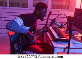 African american professional musician recording bass guitar in digital studio at home, music production technology concept.