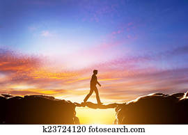 Man walking over precipice between mountains, another man being a bridge