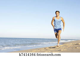 Young Man In Fitness Clothing Running Along Beach