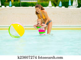 Happy mother and baby girl playing with beach ball in pool