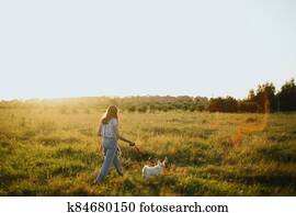 Stylish hipster girl walking with cute white puppy in summer meadow. Young woman on a walk with her doggy in warm sunshine light. Adoption concept, loyal friend Stylish hipster girl walking with cute white puppy in summer meadow. Young woman on a walk with her doggy in warm sunshine light. Adoption concept, loyal friend