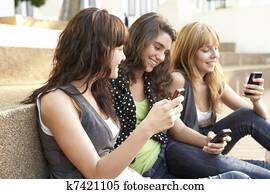 Group Of Teenage Students Sitting Outside On College Steps Using Mobile Phone Group Of Teenage Students Sitting Outside On College Steps Using Mobile Phone