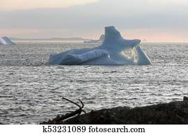 old anchor on Newfoundland rocks, iceberg in bay