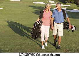 Senior Couple Walking Along Golf Course Carrying Bags Senior Couple Walking Along Golf Course Carrying Bags