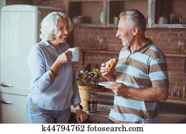 Loving smiling aged couple having breakfast in the kitchen