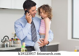 Well dressed father carrying daughter while on call in kitchen