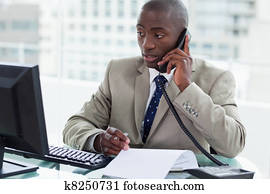 Entrepreneur making a phone call while looking at his computer Entrepreneur making a phone call while looking at his computer