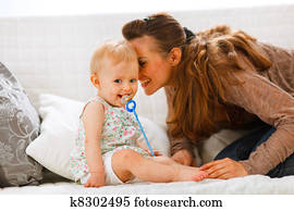 Adorable baby with soother and young mother playing on divan