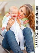 Happy mother sitting on bench in park and holding smiling adorable baby girl in hands