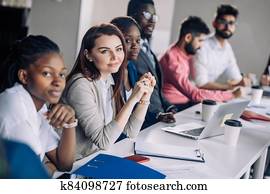Mixed race people listening to presentation sitting in row at boardroom table Mixed race people listening to presentation sitting in row at boardroom table