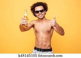 Happy young african man drinking beer showing thumbs up.