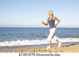 Senior Woman In Fitness Clothing Running Along Beach