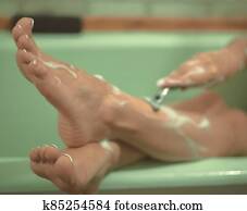 Female foots in the bathroom. The girl shaves her legs. Photo is out of focus. Female foots in the bathroom. The girl shaves her legs. Photo is out of focus.
