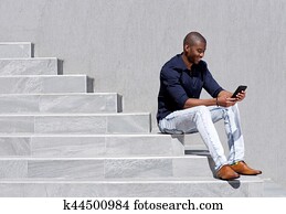 young african american man sitting on steps using tablet young african american man sitting on steps using tablet