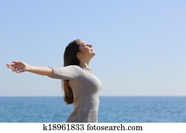 Happy woman breathing deep fresh air and raising arms on the beach