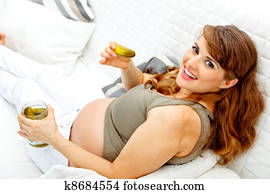 Smiling beautiful pregnant woman relaxing on sofa at home and eating pickles